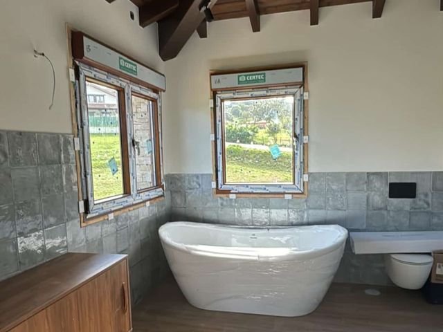 Cuarto de baño con bañera exenta, ventanas de madera y techo de vigas vistas